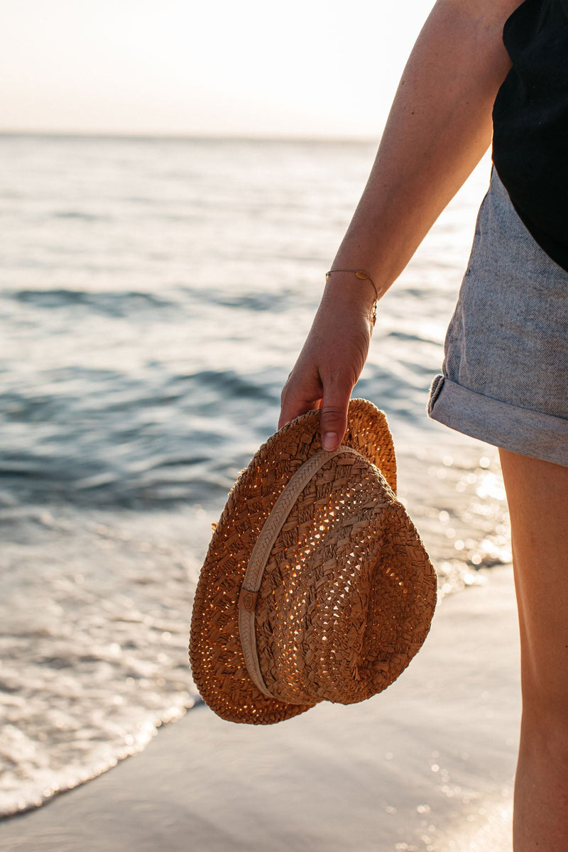 Forearm of lady carrying straw hat along beach waters edge