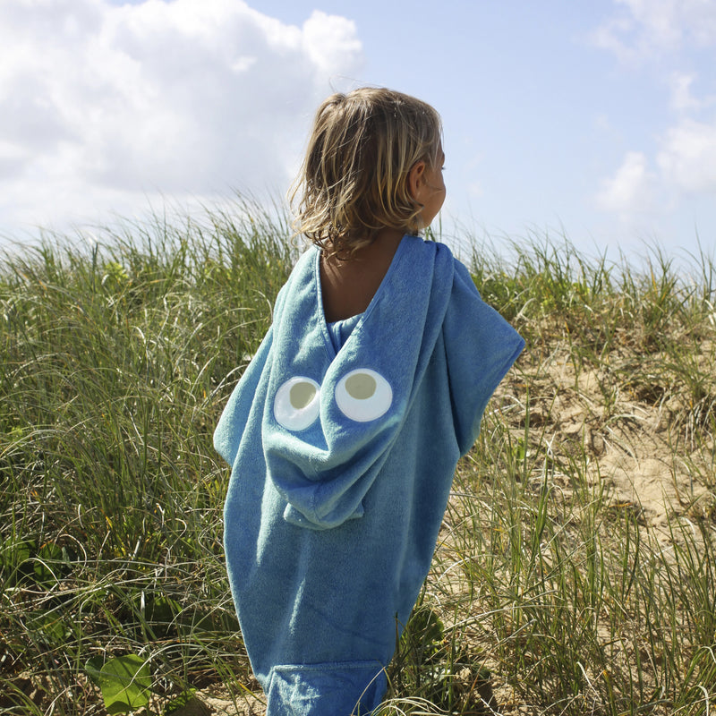 Blonde haired little boy wearing shark hooded towel waling through sand dunes