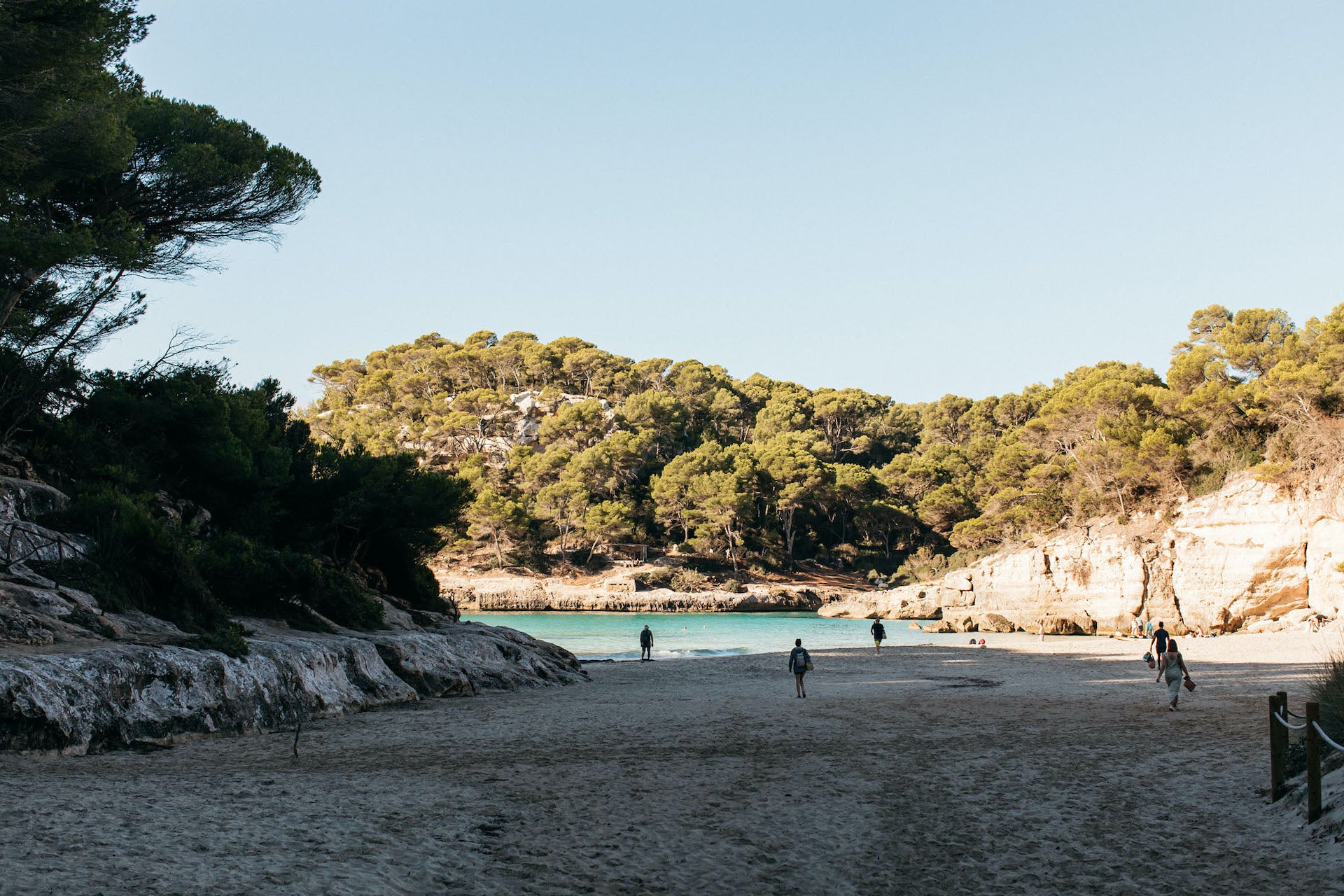 Sunlight falling on a few people strolling across a Menorcan beach